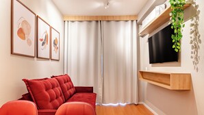 En moderne stue med en rød sofa, et tv-skab i træ og et stort vindue med gardiner.