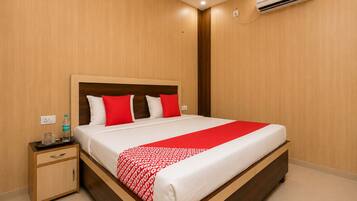 Una habitación de hotel con una cama de madera, una mesita de noche, una botella de agua y un aire acondicionado.