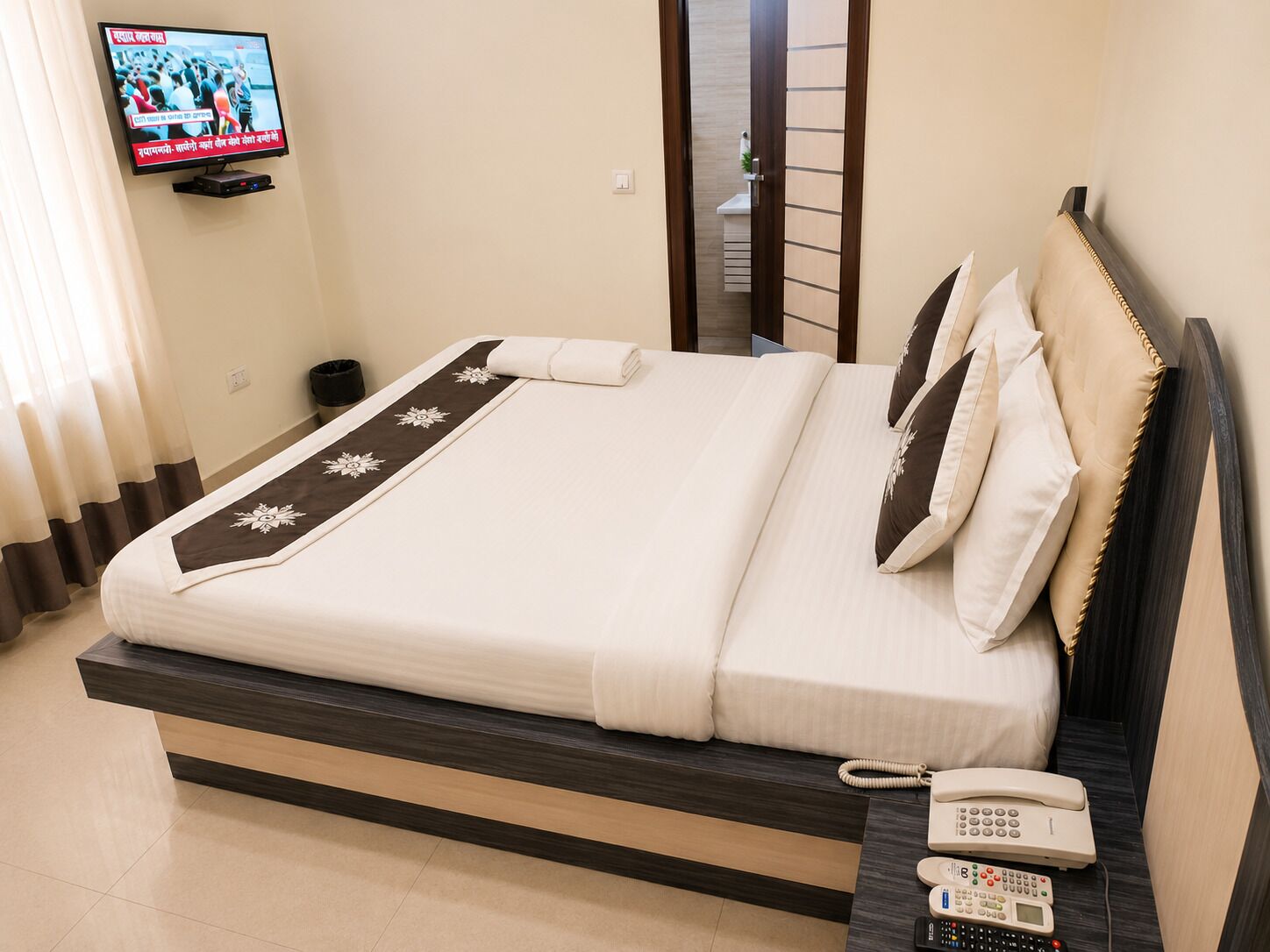 Una camera d'albergo con un letto, una TV a muro, un telefono sul comodino e una porta che dà sul bagno.