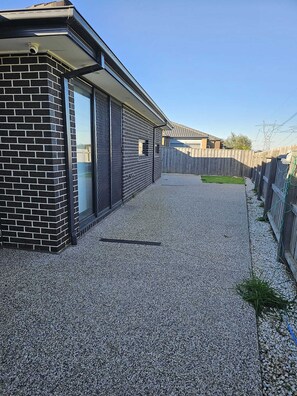 Ein Wohnhaus mit Kopfsteinpflasterauffahrt, Holzzaun und einer Ziegelmauer.