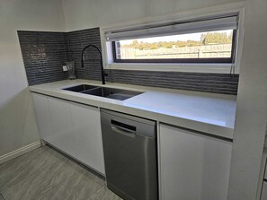 Eine moderne Küche mit Geschirrspüler, doppelter Spüle und Fenster mit Blick auf einen umzäunten Bereich.