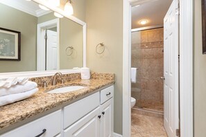 A bathroom with a granite countertop, white cabinets, a sink, and a mirror. - Phoenix Vii 71108 3 Bedroom Condo (Orange Beach)