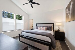 Ein Schlafzimmer mit einem Bett, Nachttischen, einem Hocker, einem Deckenventilator und einem Fenster mit Jalousien.