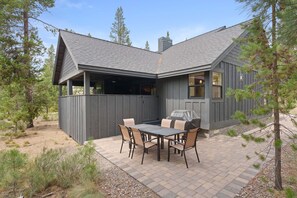 Ein Haus mit überdachter Terrasse, Grill und Esstisch mit Stühlen.