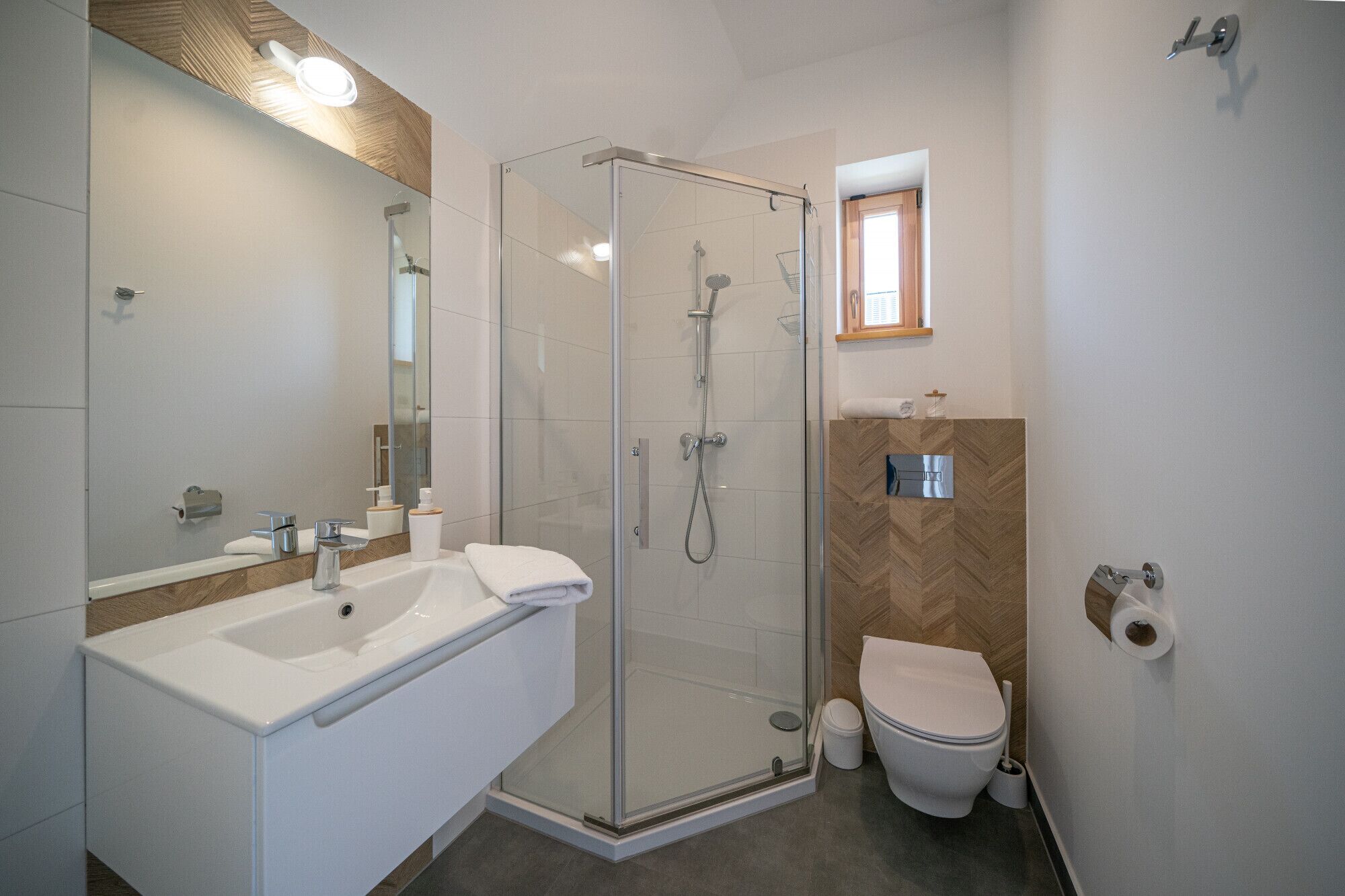 Un baño moderno con ducha de vidrio, lavamanos blanco y un inodoro.