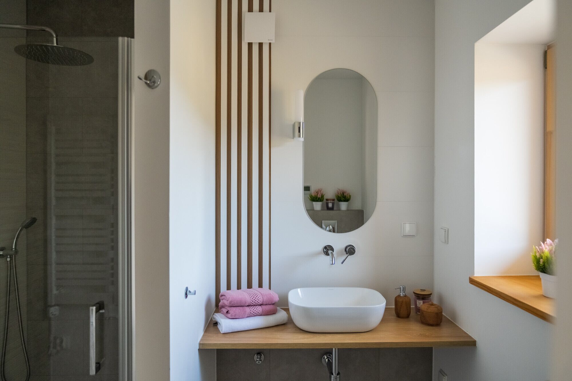 Un baño moderno con ducha, lavamanos con un espejo grande y tocador de madera.