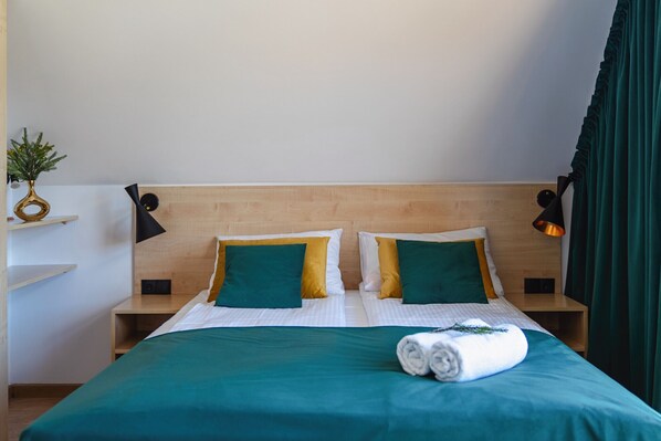 Habitación de hotel con cabecera de madera, dos mesitas de noche, cama con ropa de cama verde y una toalla enrollada sobre la cama.
