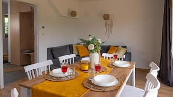 Un'area pranzo con un tavolo di legno apparecchiato per quattro, sedie bianche, un divano con cuscini e un portafortuna appeso al muro.
