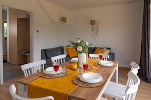 A dining area with a wooden table set for four, white chairs, a sofa with cushions, and a dreamcatcher on the wall. - Miodowe Domki (Murzasichle)