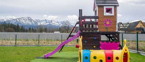 A playground with a slide, climbing wall, and a small building with a flower design.