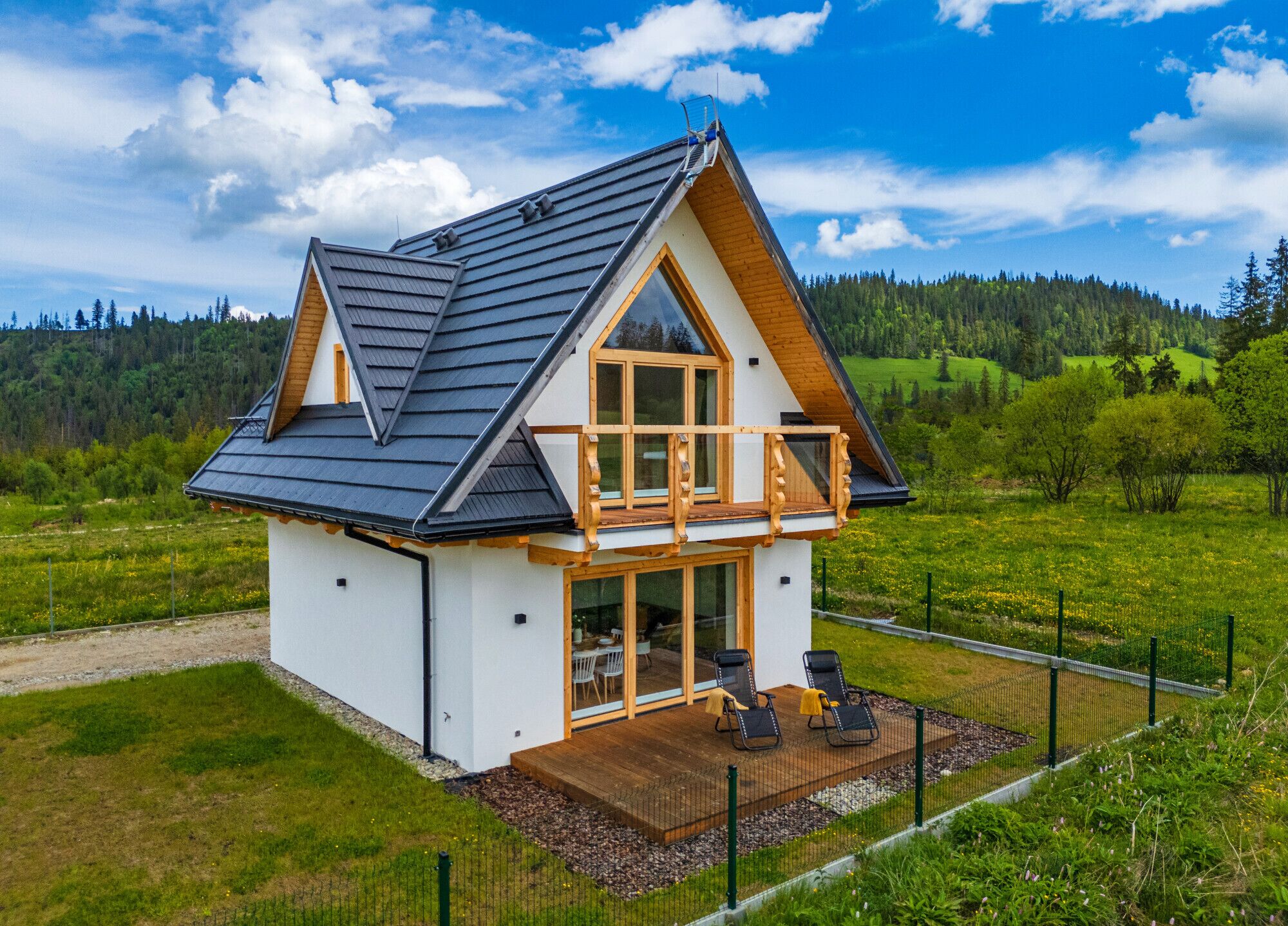A two-story house with a balcony, a wooden deck, and a view of a green landscape.