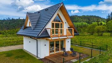 A two-story house with a balcony, a wooden deck, and a view of a green landscape.