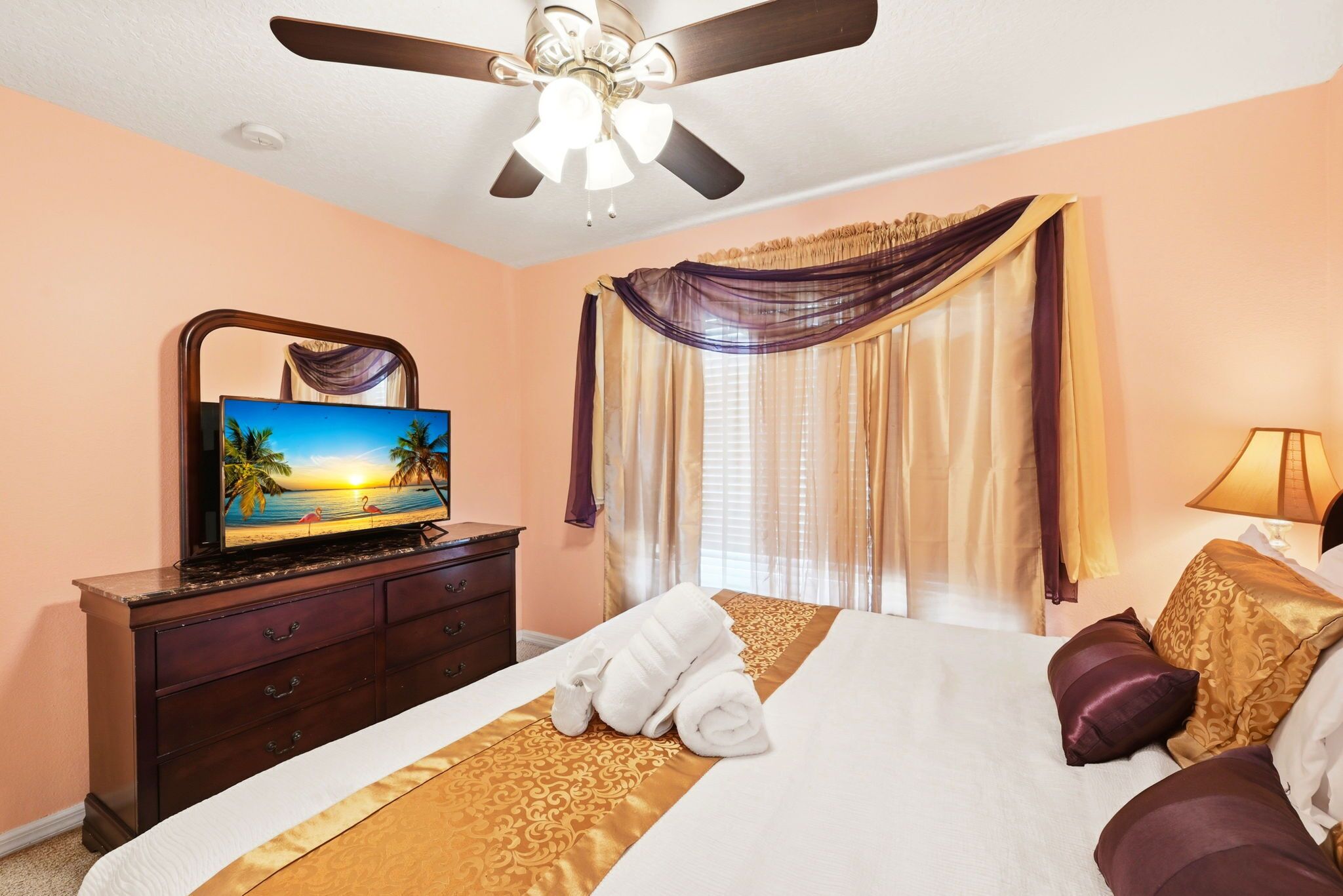 Ein Hotelzimmer mit Bett, Fernseher, Deckenventilator und einem Vorhangfenster.