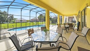 Un espace extérieur abrité, doté d’une table et de chaises en verre, d’une piscine et offrant une vue sur un quartier résidentiel.