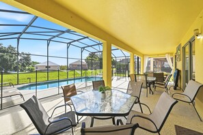 A covered outdoor area with a glass table and chairs, a pool, and a view of a residential neighborhood. - 8BR Disney Villa | Pool, W/D, WiFi, Billiards (Kissimmee)