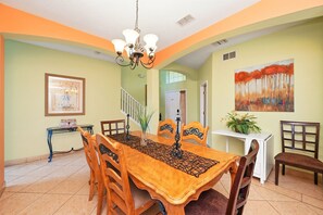 A dining area with a wooden table, chairs, a chandelier, and a painting on the wall. - 8BR Disney Villa | Pool, W/D, WiFi, Billiards (Kissimmee)