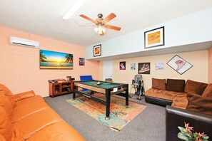 A living room with a pool table, a sofa, a ceiling fan, and wall art. - 8BR Disney Villa | Pool, W/D, WiFi, Billiards (Kissimmee)