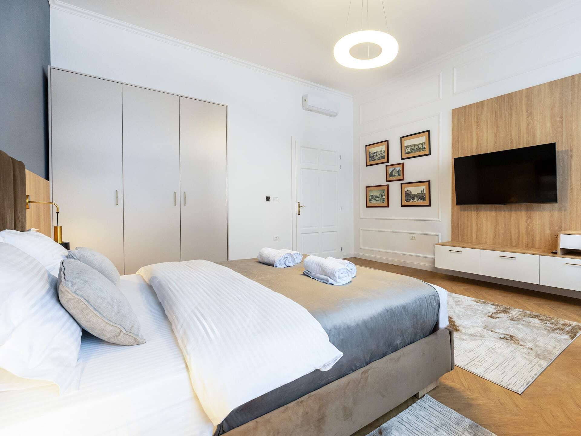 A modern bedroom with a bed, wardrobe, and a TV on the wall.