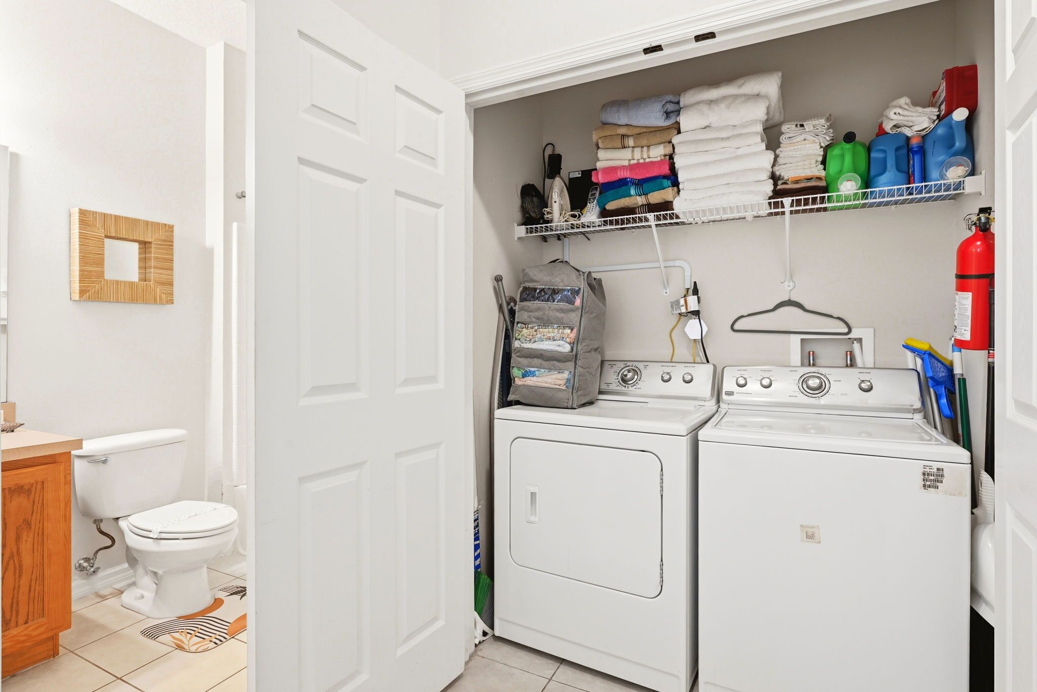 A laundry room with a washing machine, dryer, and shelves with folded towels and cleaning supplies.