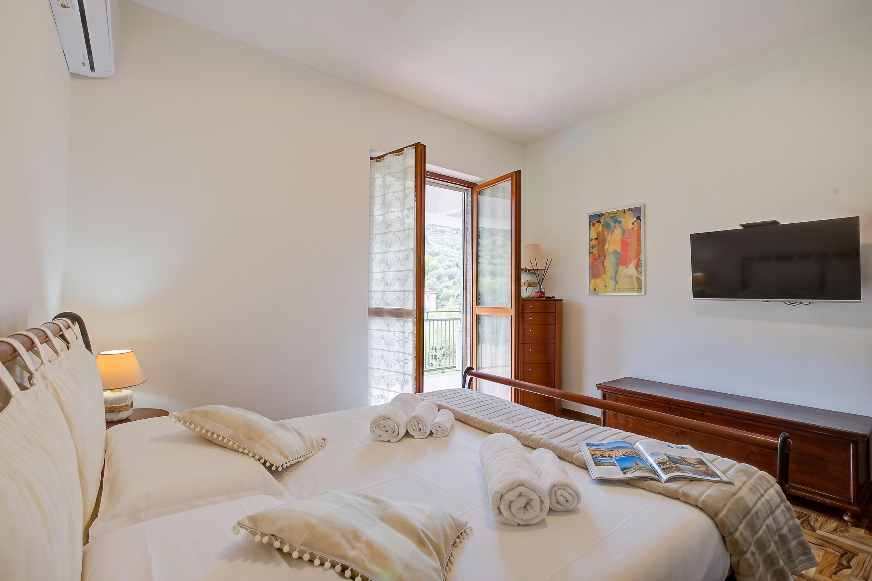 A hotel room with a bed, a desk, a television, and a window with a view of greenery.