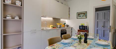 A dining area with a table set for four, a kitchen in the background, and a door with a sign.