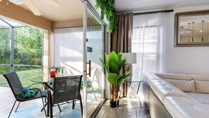 Een moderne woonkamer met een glazen deur naar een balkon, een bank, een eettafel met stoelen en een potplant.