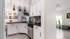Een moderne keuken met witte kasten, zwarte aanrechtbladen en hanglampen.