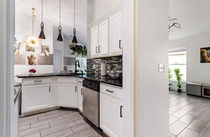 A modern kitchen with white cabinets, black countertops, and pendant lighting. - 3BR Tropical Oasis w/ Pool & Foosball near Disney (Kissimmee)