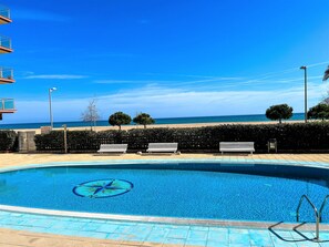 Ein Swimmingpool mit Sternenmuster, Sitzbänken, einer Hecke und Blick auf den Strand.
