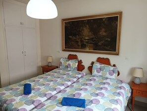 Ein Schlafzimmer mit Bett, Nachttisch, Lampe, Kleiderschrank und einem Bild an der Wand.