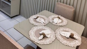 Ein modernes Hotelzimmer mit einem wandmontierten Flachbildfernseher, einem kleinen Schreibtisch mit Blumentopf und einem Essbereich mit Tisch, gedeckten weißen Tischsets und einer dekorativen Tischläufer.