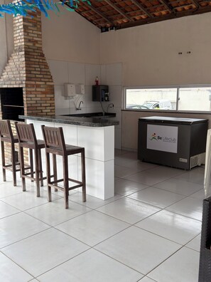 Uma cozinha com forno de tijolos, armários brancos, um espaço de bar com banquetas e uma geladeira com logotipo.