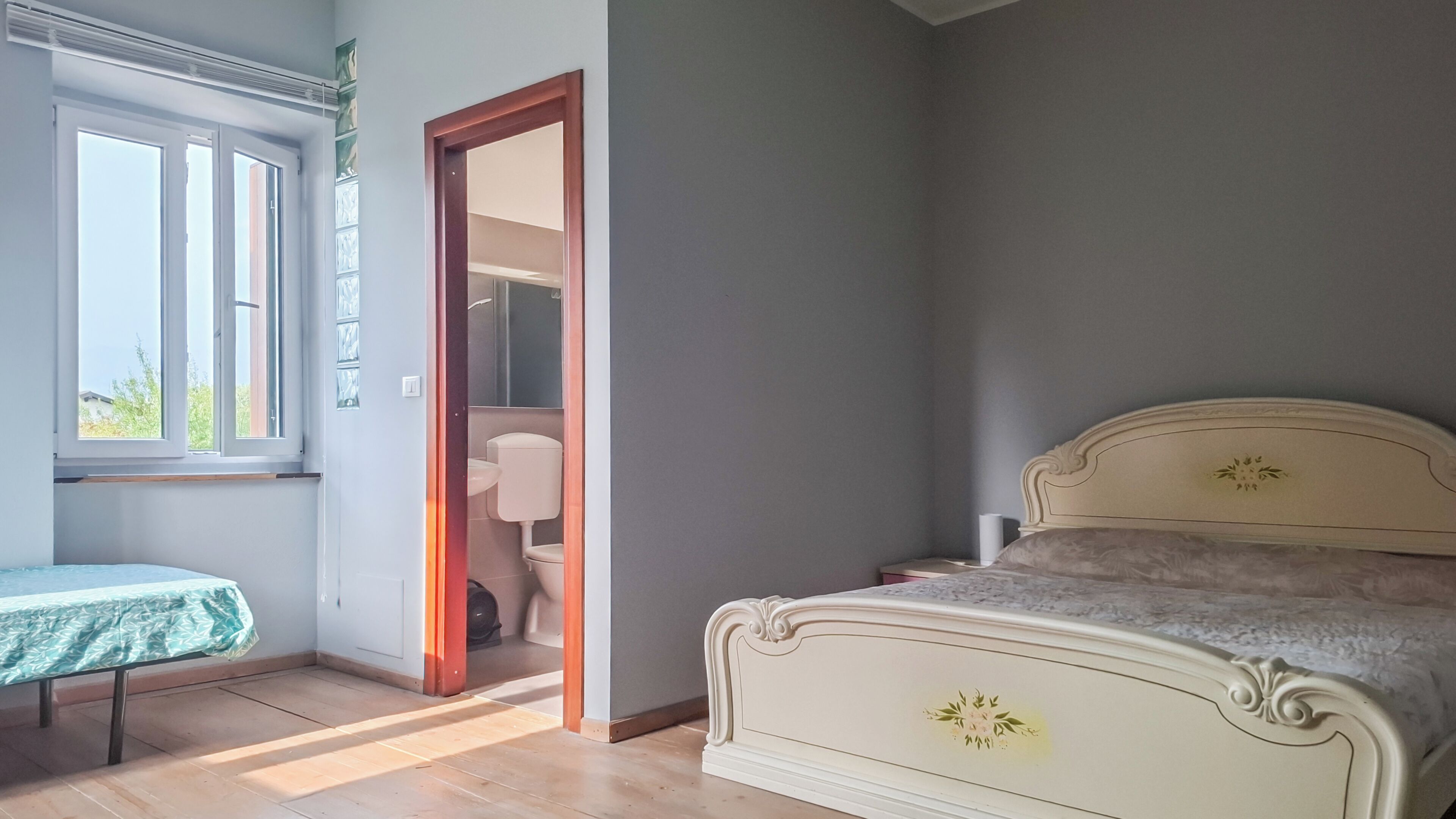 Una camera da letto con un letto, un comodino, una finestra e una porta che dà su un bagno.