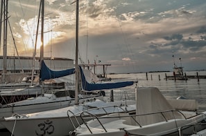 A marina with multiple sailboats docked, a pier extending into the water, and a cloudy sky.