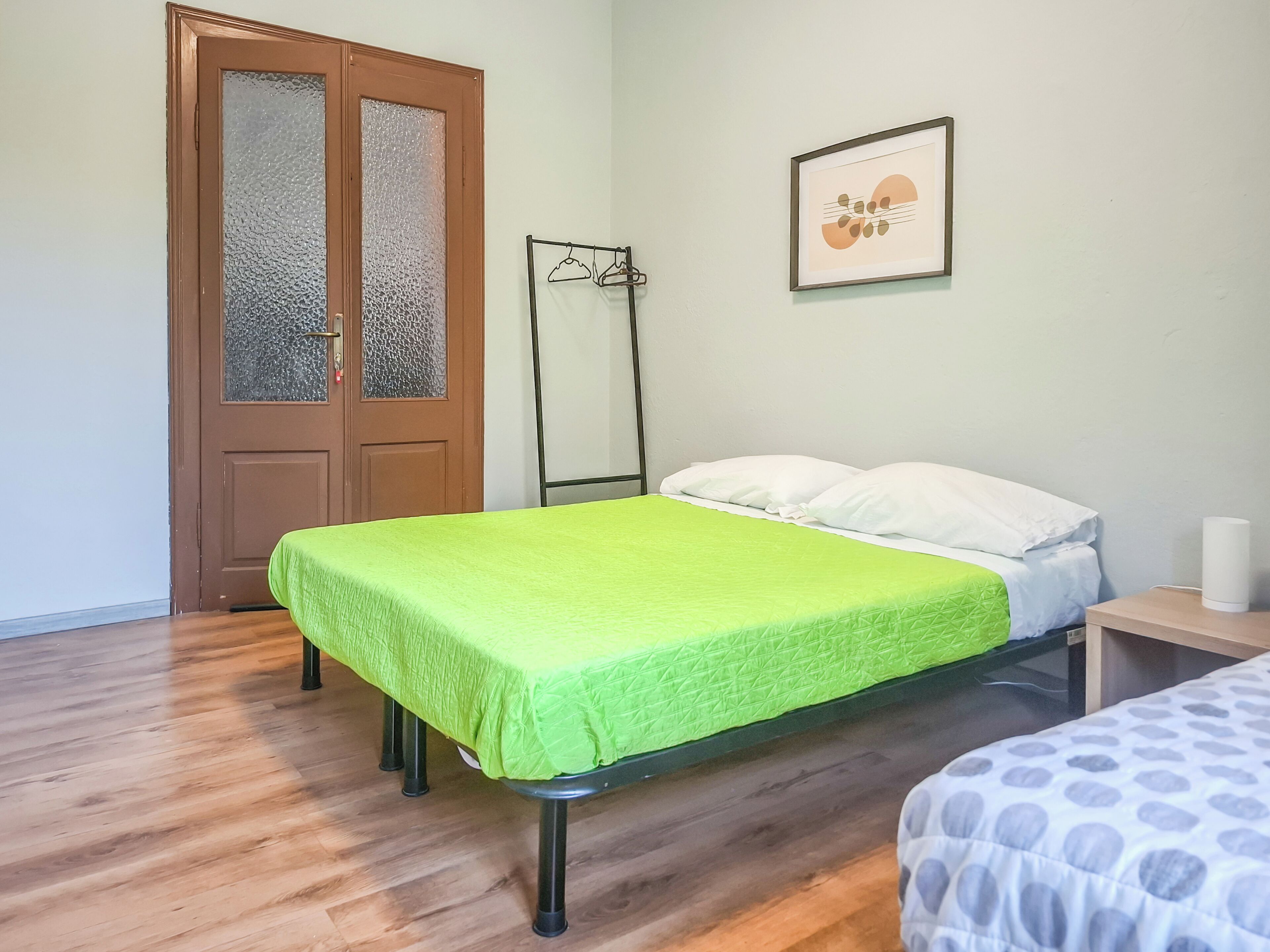 Um quarto com uma cama, uma porta de madeira, um cabideiro e um quadro na parede.