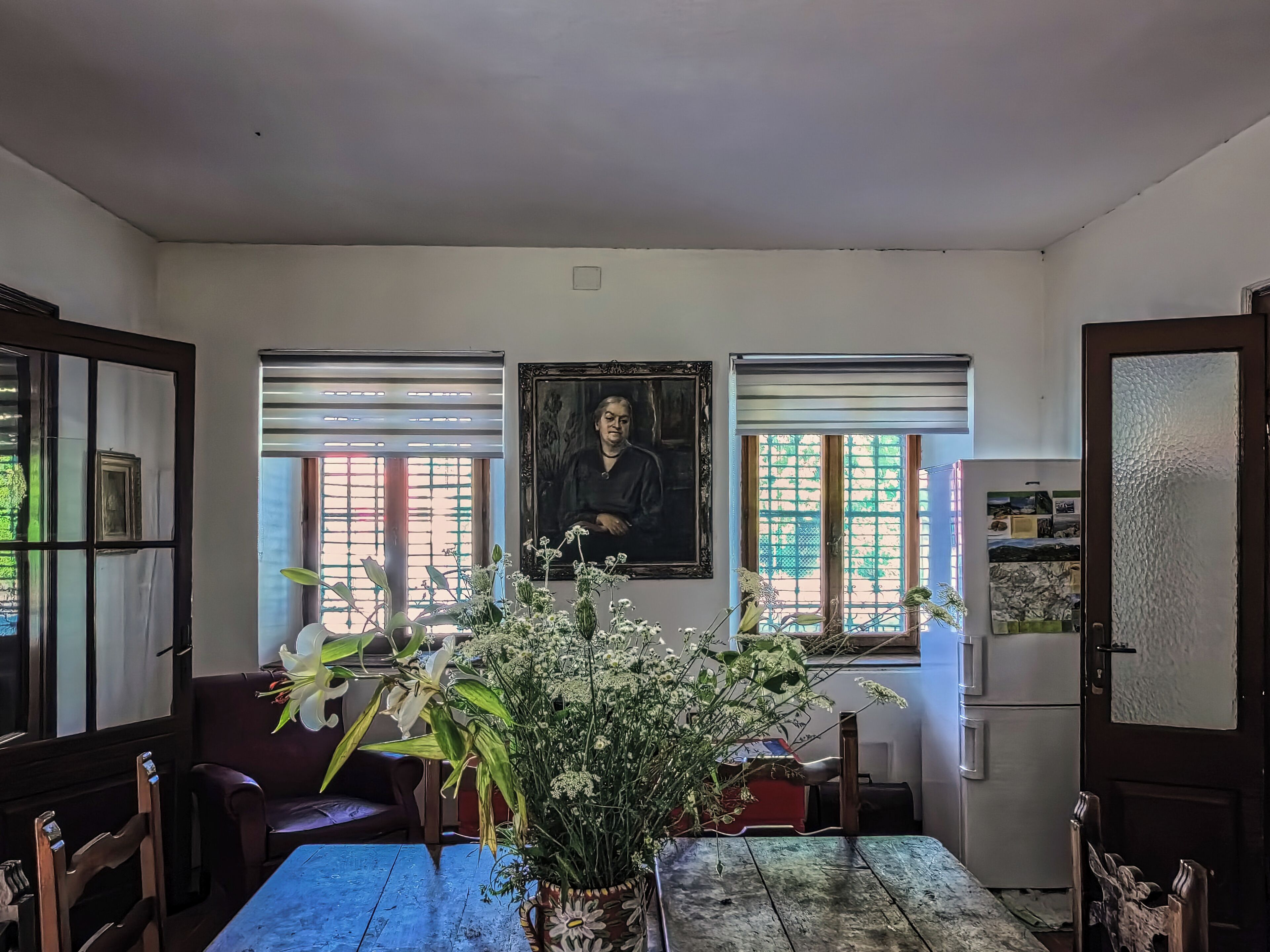 Ein Essbereich mit Tisch, Stühlen, einer Blumenvase und einem Bild an der Wand.
