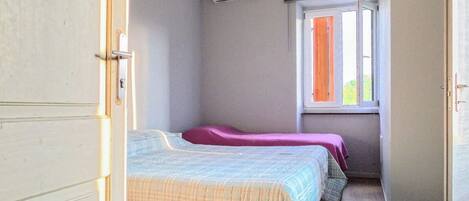 Habitación con dos camas, una ventana con cortinas, un equipo de aire acondicionado y piso de madera.