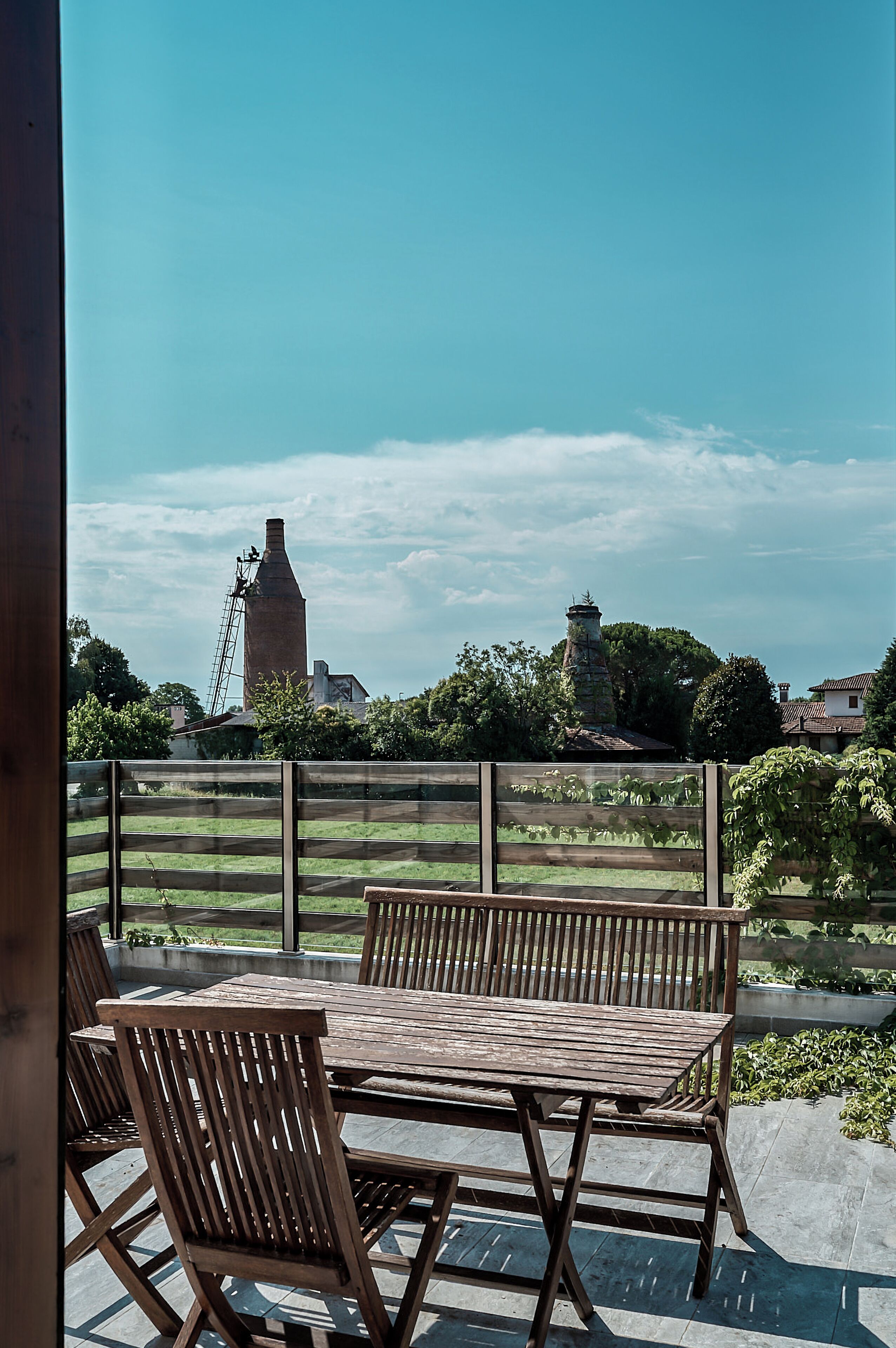Une terrasse extérieure avec une table et des chaises, une vue sur un bâtiment éloigné et un ciel dégagé.