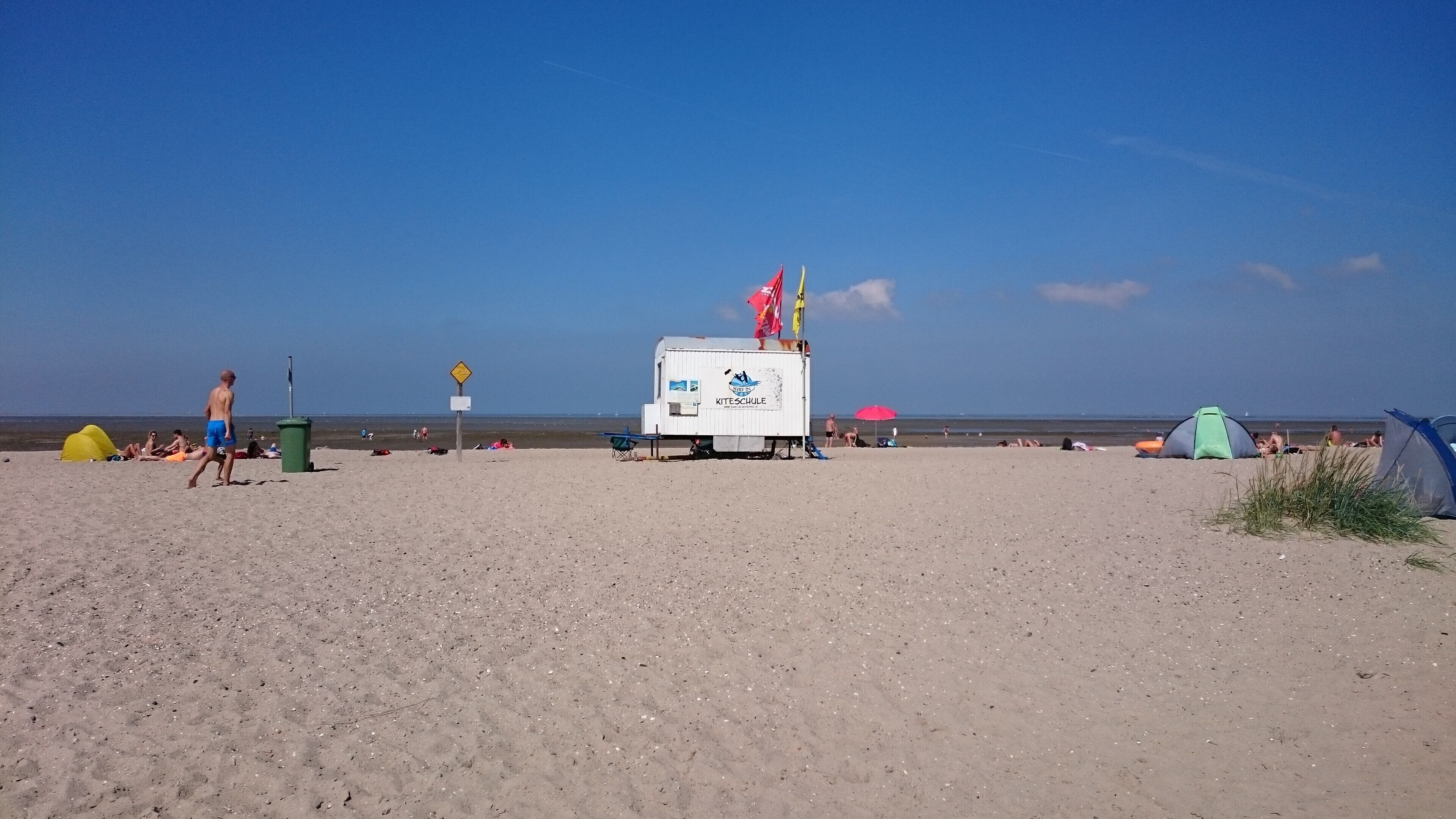 Ein Strand mit Rettungsschwimmerstation, Zelten und Menschen.