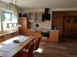 A kitchen with wooden cabinets, a dining table with chairs, a window with curtains, and a coffee maker. - Apartment 'Fewo Tenge EG Links' with Covered Terrace, Private Garden and Wi-Fi (Wangerland)