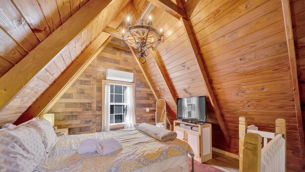 A cozy attic bedroom with a bed, a television, and a window. - Cozy Pigeon Forge Cabin Near Dollywood・Fire Pit (Pigeon Forge)