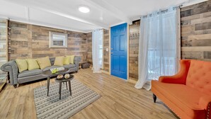 A living room with a grey sofa, a red armchair, wooden flooring, and a blue door. - Cozy Pigeon Forge Cabin Near Dollywood・Fire Pit (Pigeon Forge)