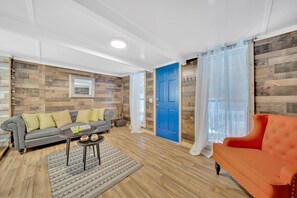 Ein Wohnzimmer mit grauem Sofa, einem roten Sessel, Holzboden und einer blauen Tür.