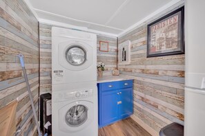 Ein Waschraum mit gestapelten Waschmaschinen, einem blauen Schrank und einem gerahmten Bild an der Wand.