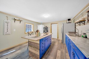 A kitchen with a central island, blue cabinets, a white refrigerator, and a wooden floor. - Pigeon Forge Single-Level Retreat Near Dollywood (Pigeon Forge)