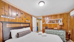 Ein Schlafzimmer mit Holz-Kopfteil, einem Bett mit weißer Bettwäsche, einer Kommode mit Schubladen und einem Spiegel darüber.