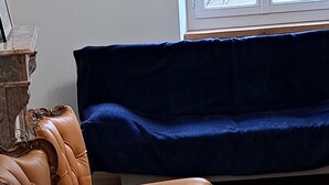 A room with a brown leather armchair, a blue sofa, and a window with a view of a building. -  grande propriété close (Polisot)