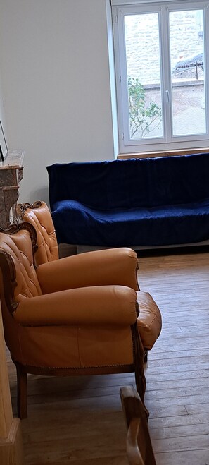 Ein Zimmer mit einem braunen Ledersessel, einem blauen Sofa und einem Fenster mit Blick auf ein Gebäude.