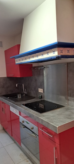 Eine Küche mit einem Edelstahl-Spülbecken, roten Schränken und einer blau-weißen Spritzschutzwand.