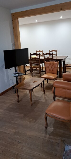 A dining area with a wooden table and chairs, a television on a stand, and a small table with a laptop and some items. -  grande propriété close (Polisot)